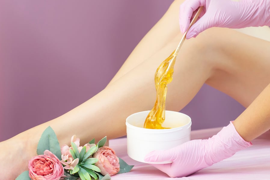 young woman having hair removal procedure on leg with sugaring paste